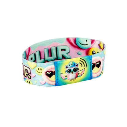 Static photo of the wristband’s back, featuring large mint-green “PLUR” text in block pixel font across a pink gradient band dotted with pastel hearts and smiley-face icons.
