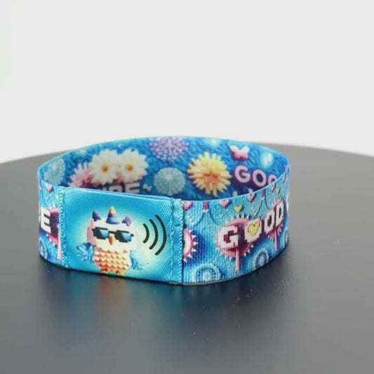 8-second rotating video of the wristband’s back, showcasing repeating ‘GOOD VIBE’ in pixel font interspersed with stylized daisy and heart motifs on a sky-blue band.